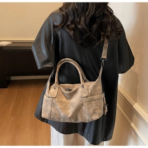 Woman in black leather jacket carrying a large vintage khaki tote bag with shoulder strap