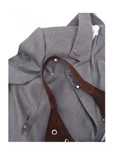 Detail of suede tote bag with metal grommets paired with a gray textured sequined blazer