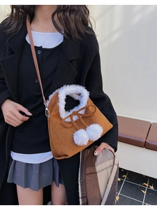 Detailed close-up of brown suede bucket bag with white faux fur trim and soft pom-pom accents