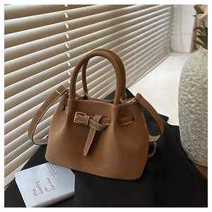 Close-up of brown frosted leather bucket bag with retro buckle detail in a cozy setting