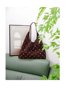 Close-up of brown suede shoulder bag with gold metal grommets on a leather sofa