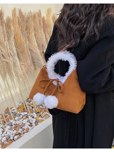 Close-up of a brown suede bucket bag featuring white faux fur trim and cute pom-poms