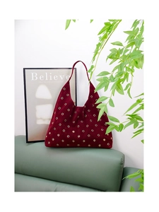 Close-up of a burgundy suede Hobo bag with gold rivets on a green leather sofa