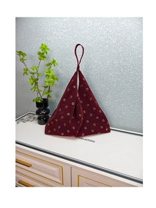 Detail of burgundy velvet tote bag featuring decorative gold eyelets and triangular shape