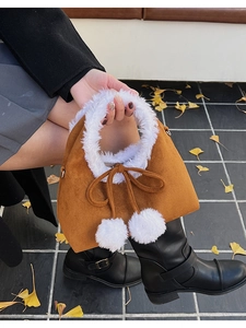 Detail of a brown suede bucket bag with white plush fur trim and oversized fuzzy pompoms