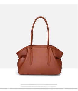 Detail of a brown leather tote bag showing unique pleated sides and slim shoulder straps