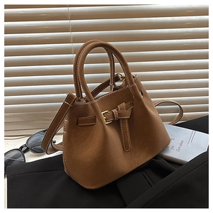 Detail of caramel suede bucket bag with gold buckle on a textured black background