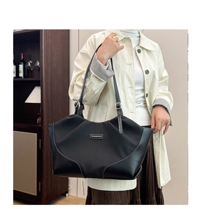 Macro detail of large black tote bag with white contrast stitching and metallic logo