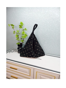 Detail of black suede triangular handbag featuring decorative gold metal eyelets