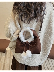 Close-up of brown suede bucket bag with white faux fur trim and fluffy pompom charms