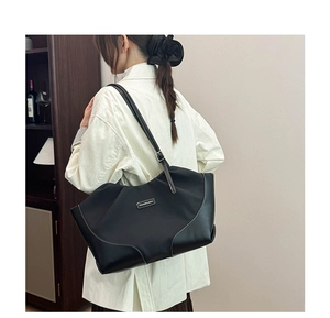 Detail of high-capacity black tote bag featuring white contrast stitching and metal logo