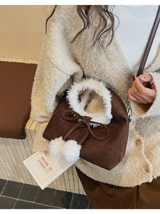 Detailed close-up of dark brown suede bucket bag with white faux fur trim and pom-poms
