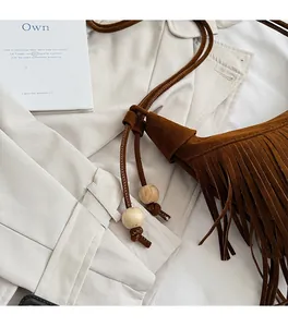 Macro view of dark brown suede bag featuring long fringe and decorative wooden beads