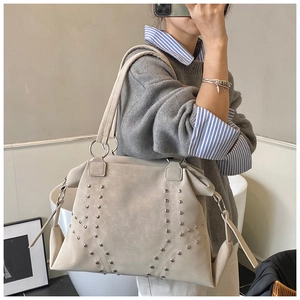 Sac fourre-tout beige élégant avec rivets argentés porté par un mannequin au décor épuré