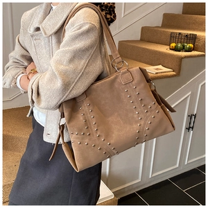 Detail of tan faux suede tote bag featuring symmetric silver studs and decorative ribbons