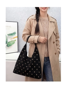 Detail of a black suede hobo bag with metal grommets worn with a stylish trench coat
