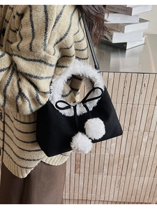 Detail of plush faux fur trim and white pom-poms on a black bucket tote bag