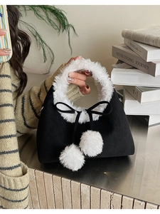 Close-up of black suede bucket bag featuring white faux fur trim and dual pom-pom charms