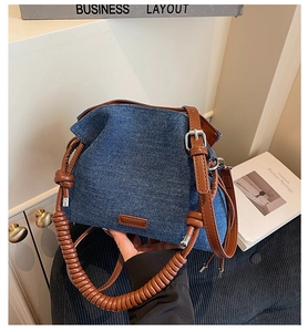 Detail of blue denim bucket bag featuring brown leather spiral handle and silver hardware