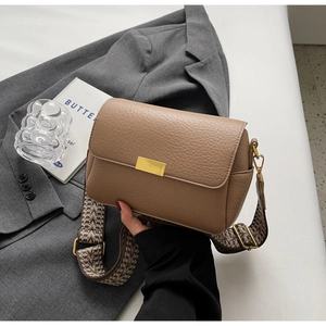 Detail of lychee pattern leather texture and gold buckle on a brown crossbody bag
