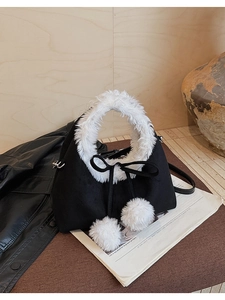 Detail of plush black bucket bag with white faux fur trim and decorative pom-poms