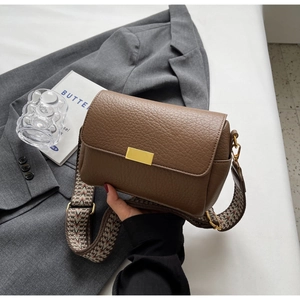Close-up of brown pebbled leather flap bag featuring gold clasp and colorful woven strap