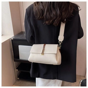 Detail of the litchi grain texture and gold metal buckle on a cream crossbody bag