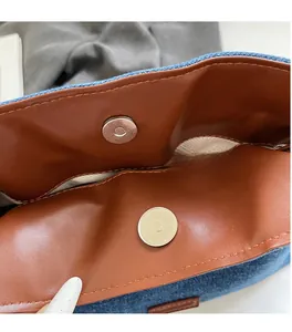 Detail of magnetic silver hardware and brown leather lining on a denim bucket bag