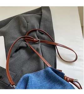 Detail of adjustable brown leather strap and silver buckle on denim bucket bag