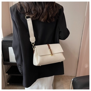 Detail view of off-white lychee grain crossbody bag with wide strap on a blazer model