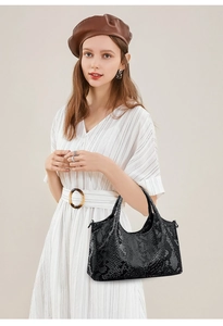 Detail of black snake-embossed leather handbag with dual handles and metallic hardware