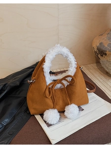 Detail of caramel suede bucket bag featuring white faux fur trim and cute pom-pom bows