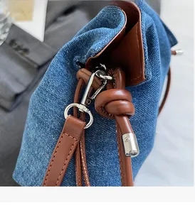 Detail of silver polished metal hook and brown leather trim on blue denim handbag