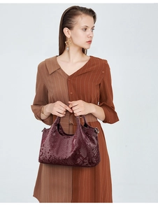 Detail of burgundy snakeskin embossed faux leather handbag with a curved top handle