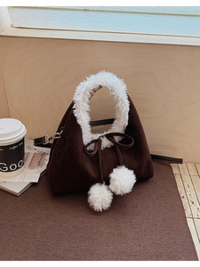 Detail of dark brown suede bucket bag with white faux fur handle and plush pom-pom charms