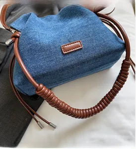Detail of blue denim handbag with spiral wrapped brown leather handle and silver buckle