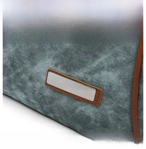 Detail of grey-blue canvas backpack with silver metal plaque and brown leather trim