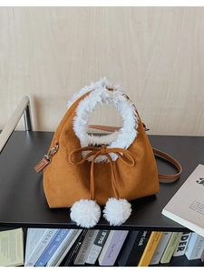 Detailed view of the brown suede bucket bag featuring white faux fur trim and pom-poms