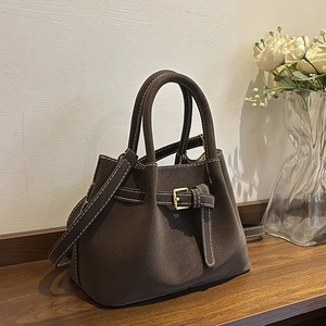 Brown bucket bag with white stitching and metal buckle on dark wood background