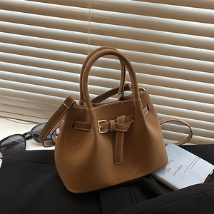 Brown suede bucket handbag with gold buckle and adjustable strap in natural lighting