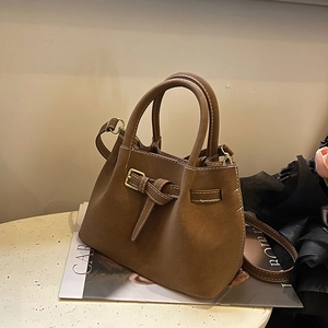 Brown suede bucket bag with white stitching and metal buckle detail on a magazine