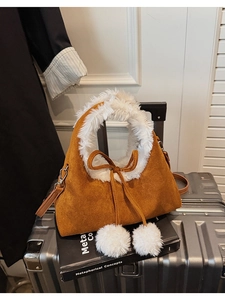 Close-up of brown suede bucket bag featuring white faux fur trim and fluffy pom-pom charms