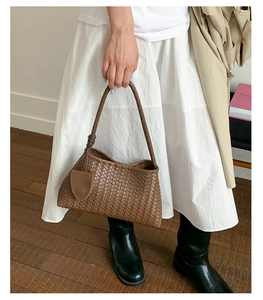 Detail of dark brown woven tote bag with Intrecciato leather texture and a shoulder strap