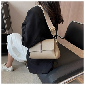 Close-up of khaki crossbody bag with wide strap and gold metal buckle shown on model