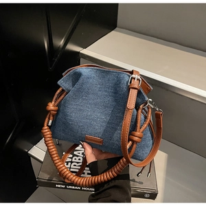Detailed close-up of dark blue denim bucket bag featuring a brown leather coil-wrapped handle