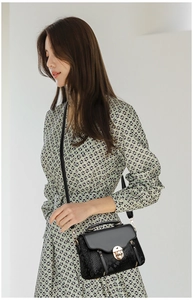 Detail of black crossbody bag with snake-embossed leather and golden metal clasp