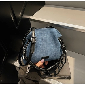 Close-up of blue denim dumpling bag with black woven handle and leather shoulder strap