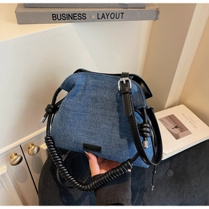 Detail of blue denim bucket bag with unique black spiral handle and leather strap