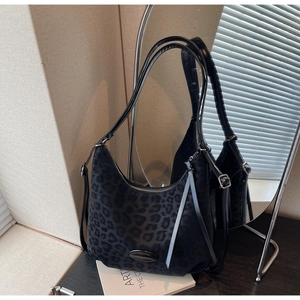 Detail of black leopard print hobo bag with dual straps and silver zipper on dark wood