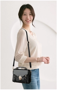 Detail of black crossbody bag with snakeskin texture and gold buckle on a model